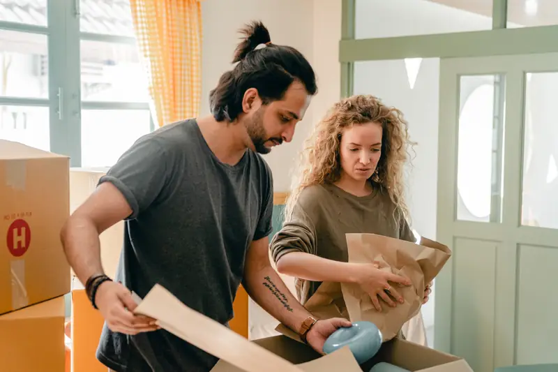 Two people wrap a piece of crockery in paper before placing it in a box.